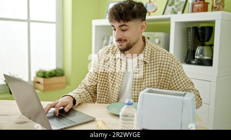 Young arab man having breakfast using laptop at home Stock Photo
