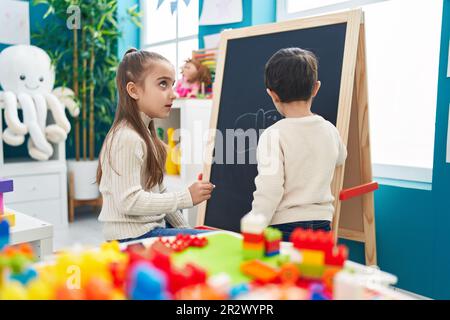 Adorable boy and girl preschool students drawing on blackboard at kindergarten Stock Photo