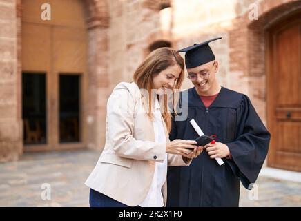 Man and woman mother and graduated son using smartphone at university Stock Photo