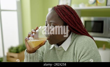 African woman with braided hair drinking juice at dinning room Stock Photo
