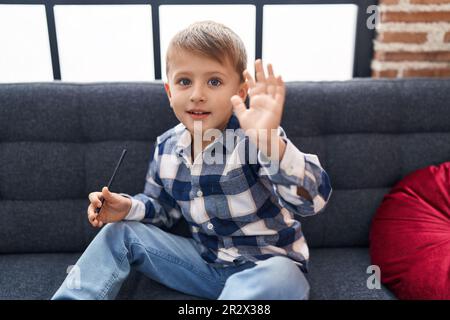 Adorable caucasian boy saying hello with hand sitting on sofa at home Stock Photo