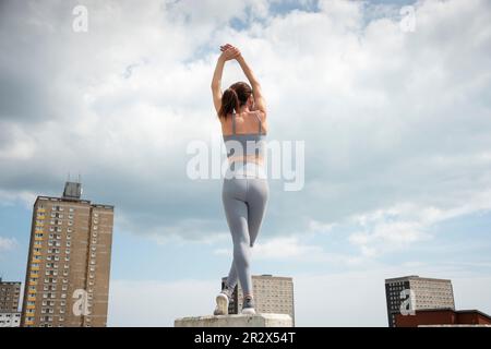 fit, sporty woman doing an arm stretch outside, outdoor exercise, urban setting. Stock Photo