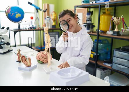 Adorable hispanic girl scientist student using magnifying glass at laboratory classroom Stock Photo