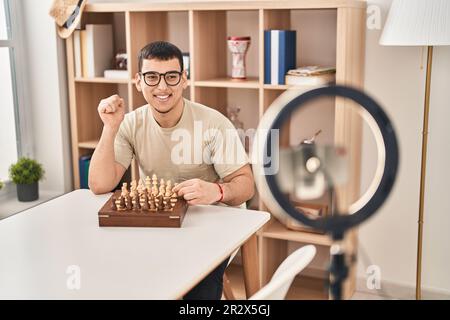Young arab man doing chess tutorial screaming proud, celebrating victory and success very excited with raised arm Stock Photo