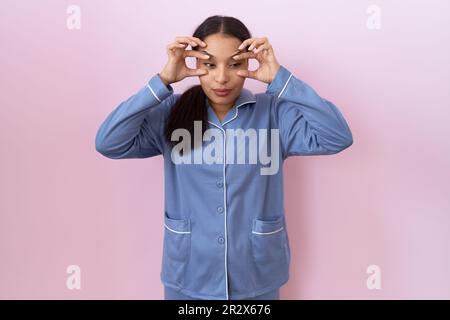 Young arab woman wearing blue pajama trying to open eyes with fingers, sleepy and tired for morning fatigue Stock Photo