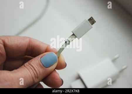 Broken electric plug in hand. Broken power cord in woman hand. Broken usb cord. Smartphone device. Cable for mobile phone. Stock Photo