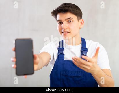 Man in blue jumpsuit shows dark empty mobile phone screen and points at device with his hand Stock Photo