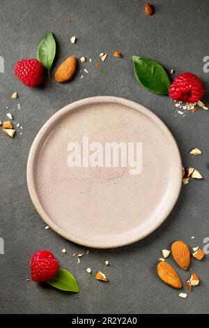 empty pink plate on grey kitchen table with raspberries and almonds for serving ice cream or dessert, top view Stock Photo