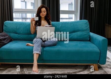 Focused young woman using her portable computer while sitting on the cozy sofa in the room during the tea break Stock Photo