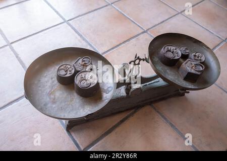 an antique scale with weights of different sizes on both sides, on a rustic floor,old weight, antique vintage balance, old scales on a tile surface, s Stock Photo
