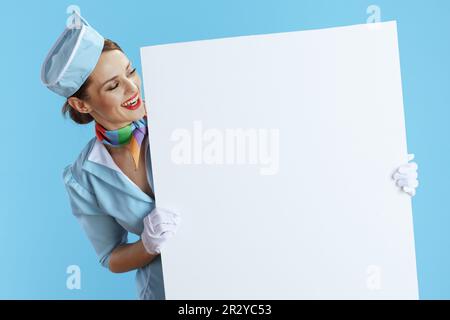 happy stylish air hostess woman isolated on blue background in blue uniform showing blank board. Stock Photo