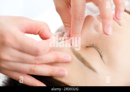 Close-up of a woman and her practitioner's hands being given acupuncture needles on her face in an acupuncture clinic. Stock Photo