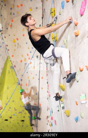 Determined young man doing his best at climbing artificial wall Stock Photo