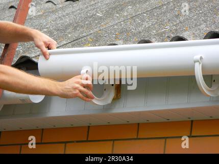 Rain gutter installation. Repair and renovate rain gutter pipeline on old house with asbestos rooftop. Stock Photo