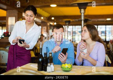 Couple using smartphones to order food in restaurant Stock Photo