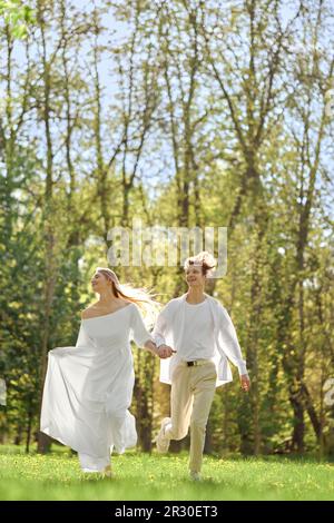 Happy newlyweds holding hands and running across the lawn in sunny day Stock Photo