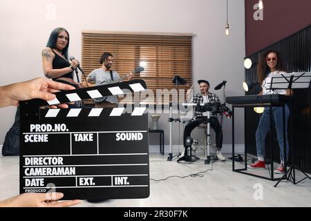 Shooting movie. Second assistant camera holding clapperboard in front of band (actors) at studio (film set) Stock Photo