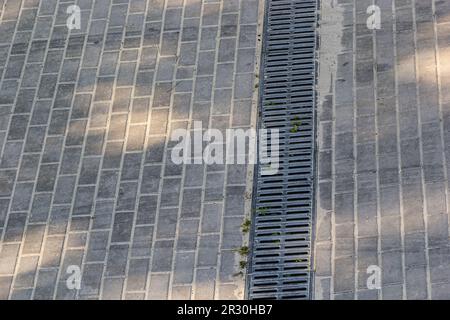 A lattice of a drainage paving system on a footpath made of square stone tiles, close up of a rainwater drainage system. Stock Photo