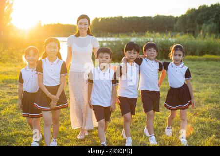 Cheerful Chinese school children relaxing in park with their teacher ...
