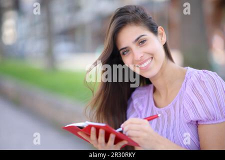 Happy woman writing in paper agenda looks at you in the street Stock Photo