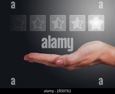 Hand holds five-star rating icons on dark gradient background Stock Photo