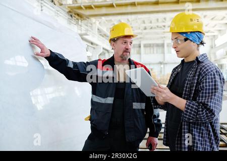 Two colleagues using digital tablet while discussing the material for production standing in workshop Stock Photo