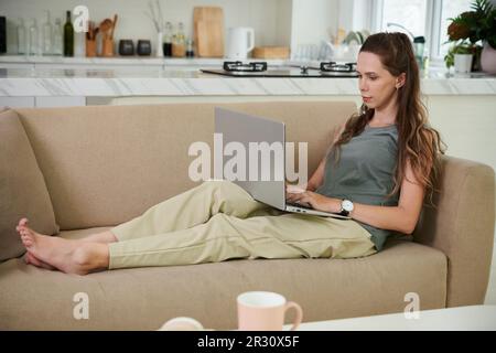 Young businesswoman sitting on couch and working on laptop Stock Photo