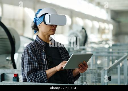 Female engineer connecting tablet pc with VR glasses and using them in her work in factory Stock Photo