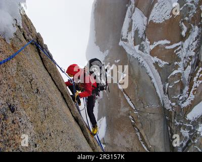 An alpinist climbs on the north face of Punta Herron, with the ice-coated granite wall of Cerro Standhardt  in the background. Stock Photo