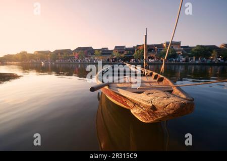 Close-up wooden boat moored against busy waterfront ancient city Hoi An at sunset. Popular tourist destination in Vietnam. Stock Photo