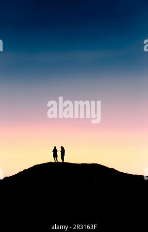 The silhouette of two people standing on an ancient bronze age bowl barrow on Barrowfields in Newquay in Cornwall in the UK. Stock Photo