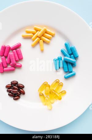 Food supplements of bright color lie on a white plate on a blue background. Concept of health support and lack of vitamins. Vertical photo Stock Photo