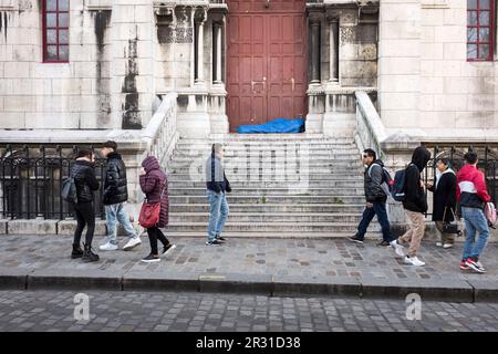 Tourists walk by a homeless person sleeping in a blue sleeping bag on the steps at the side of The Basilica of Sacré Coeur de Montmartre, Sacred Heart of Montmartre, in Paris, France. Stock Photo