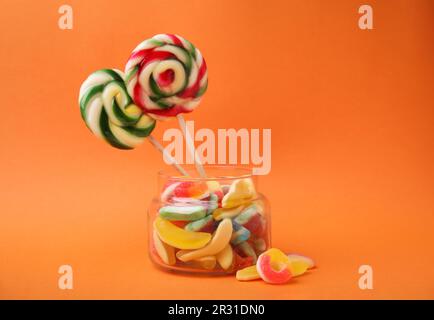 Tasty jelly candies and lollipops in jar on orange background Stock Photo