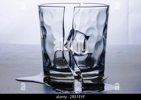 Broken glass glass in two halves with three ice cubes. Photographed on white background in study. Backlight still life. Stock Photo