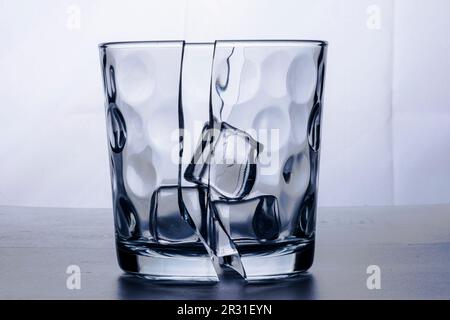 Broken glass glass in two halves with three ice cubes. Photographed on white background in study. Backlight still life. Stock Photo