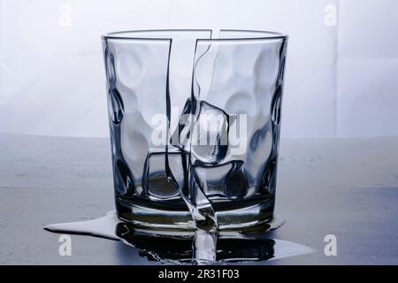 Broken glass glass in two halves with three ice cubes. Photographed on white background in study. Backlight still life. Stock Photo