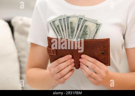 Woman holding brown leather wallet with dollar bills indoors closeup. Money exchange Stock Photo