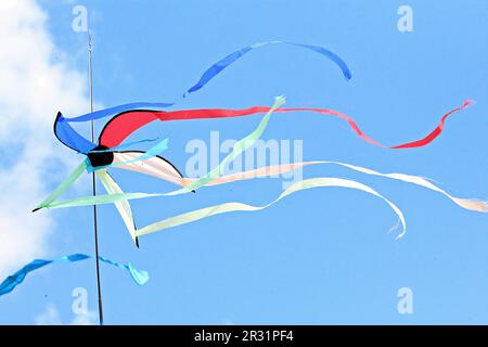 red, white, blue and green Kite with streamers blowing in the wind with a clear blue sky and one white cloud Stock Photo