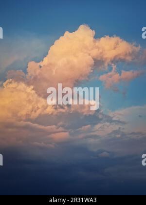 Sunlit cumulus storm clouds, pink and golden sunset light. Dreamy sky, vertical celestial background Stock Photo
