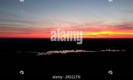 A captivating sunset sky casts its warm hues over a tranquil lake, with the moon and a lone star adding a touch of enchantment. Stock Photo
