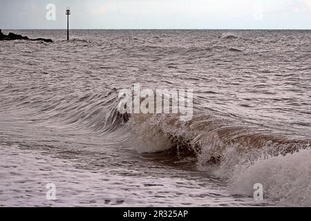 storm waves churning the sea at Sidmouth, Devon with a market post in the background and stormy skies Stock Photo