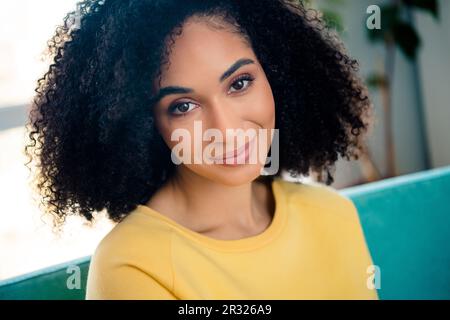 Portrait of good mood pleasant adorable girl with wavy hairstyle dressed yellow stylish sweatshirt looks in your eyes indoors room Stock Photo