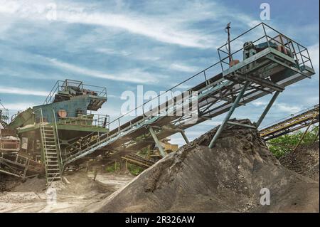 Crushing machinery, cone type rock crusher, conveying crushed granite gravel stone in a quarry open pit mining.. Minning industry gravel quarry convey Stock Photo