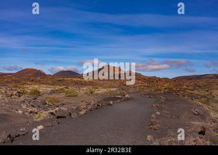 Winding road leading to mountains. Sandy-clay soil. Mountain landscape under white clouds. Stock Photo