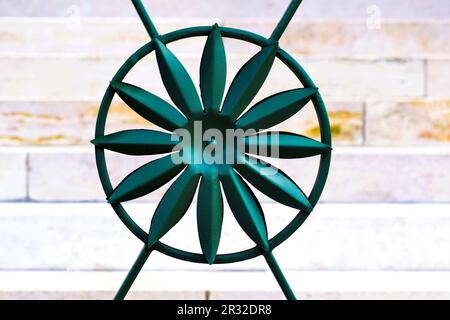 isolated green color wrought iron fence closeup detail. rose flower shaped decorative circular element. steel bar pickets. soft beige color stone wall Stock Photo
