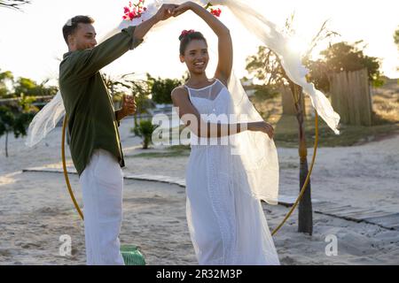 Happy diverse bride and groom dancing at their beach wedding Stock Photo