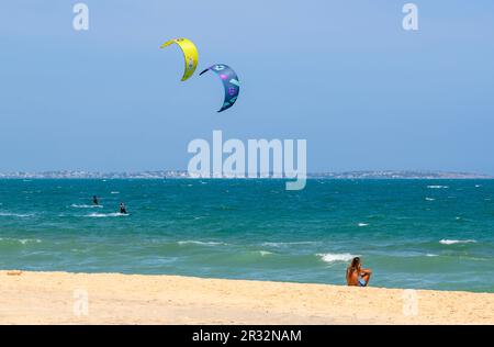 A local man sits alone on the beach observing the kitesurfers in action at sea in Mui Ne, Vietnam. Stock Photo