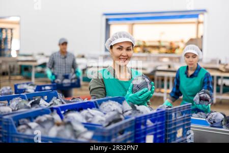 Smiling female employee of vegetable sorting factory arranging red ...