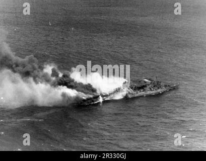 The U.S. aircraft carrier USS Franklin (CV-13) pictured burning in the waters off Japan after being hit during an air attack on 19 March 1945. The light cruiser USS Santa Fe (CL-60) is alongside. The photo was taken by planes from the USS Essex (CV-9) returning from a strike on Kobe, Japan. When Japan was facing defeat in late 1944 it chose to destroy US ships with suicide bombings, known as Kamikaze.These attacks were a potent physical and psychological weapon and sunk a total of 47 ships at a cost of more than 3000 pilots and planes. By late 1944 the US Navy was large enough that the losses Stock Photo